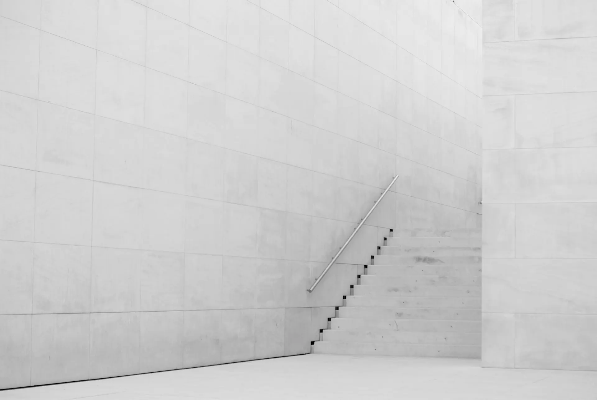 White concrete stairs rising along a bare wall, lit from above